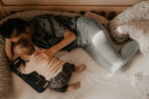 une jeune maman est allongee sur le lit a cote de son bebe qui regarde un livre