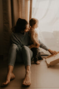 un bebe assis contre sa maman sur le sol du salon