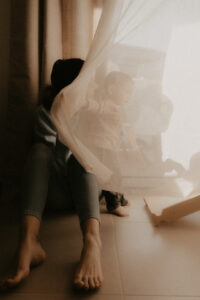 un bebe joue avec le rideau du salon a cote de sa maman