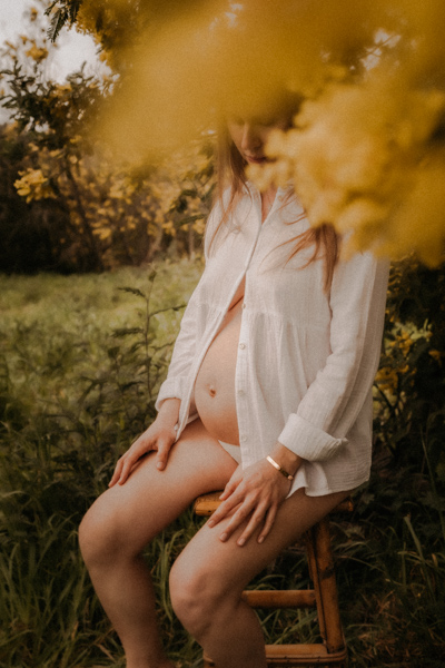 une femme enceinte est assise sur un tabouret devant du mimosa