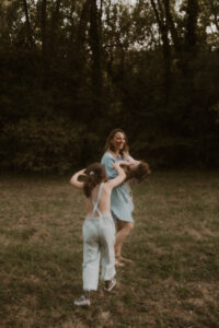 une grande soeur va chatouiller son petit frere dans les bras de leur maman