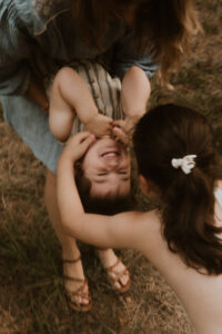 une grande soeur chatouille son frere dans les bras de sa maman