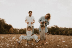 des enfants suspendus aux bras de leurs parents dans un champs de fleurs a vaugrenier