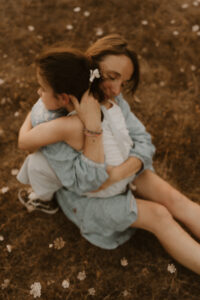 une maman sert sa fille contre elle assises dans herbe
