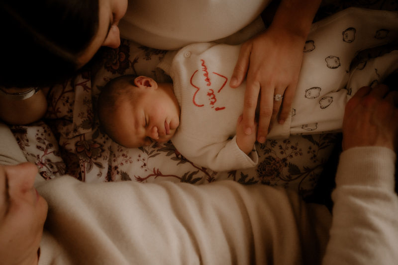 un nouveau-ne dort entoure de ses parents sur le lit de leur maison pendant une seance photo naissance