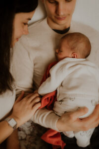 de jeunes parents prennent le temps de caliner leur bebe contre eux pendant leur seance photo lifestyle naissance a la maison