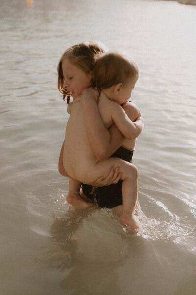 en seance photo une fille porte sa petite soeur dans les bras dans la mer a menton
