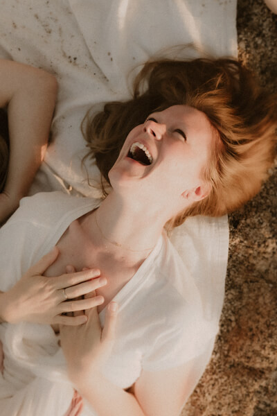 une femme rigole allongee sur le sable a menton