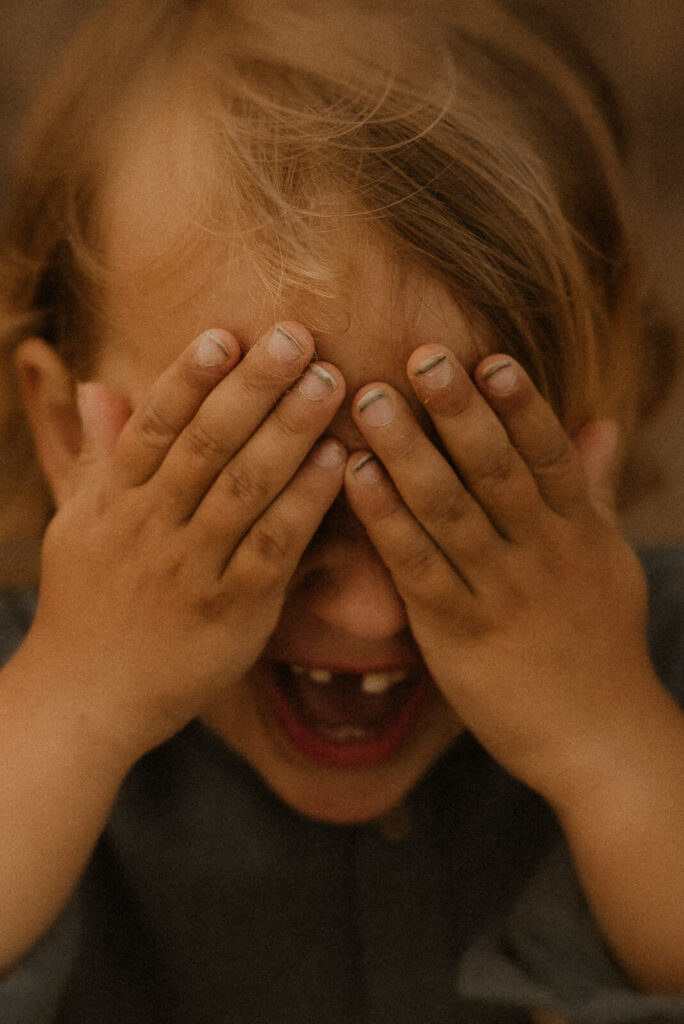 un enfant se cache les yeux avec ses mains